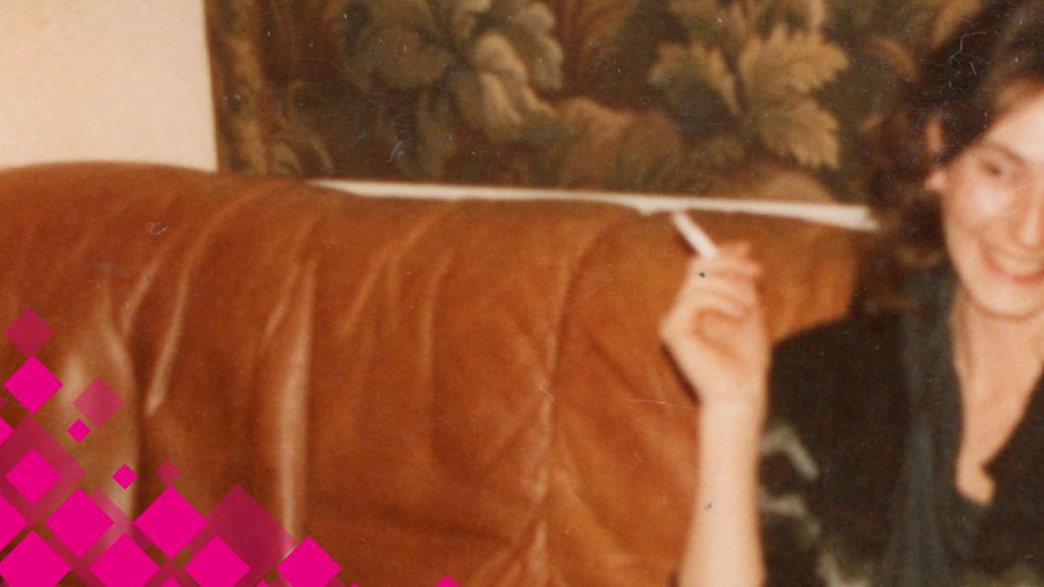 Une femme assise dans un fauteuil en cuir fume une cigarette. La photo est vieillie et ternie.