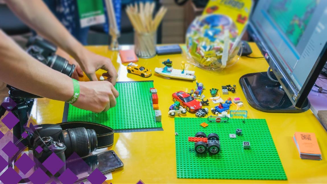 Des mains assemblent des constructions en Lego. Un appareil photo est posé à côté.